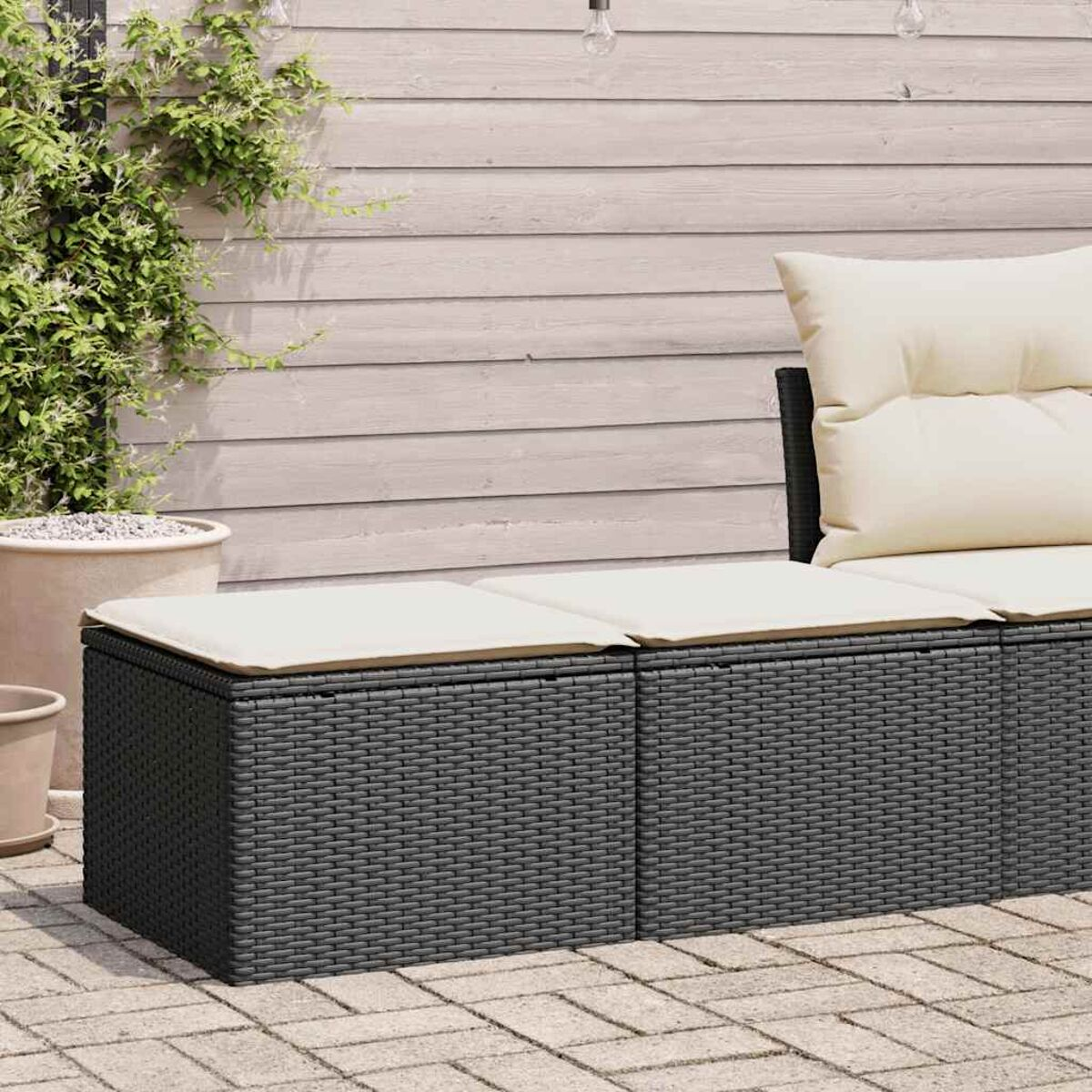 Divano in vimini grigio scuro con cuscini beige. Il divano è su un patio in pietra.