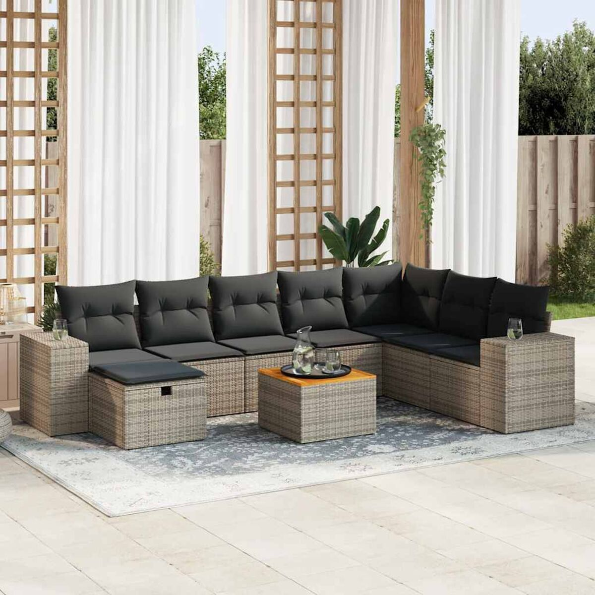 Graues Rattan-Sofa mit schwarzen Kissen, Tisch mit Getränken und Vorhängen auf Terrasse.