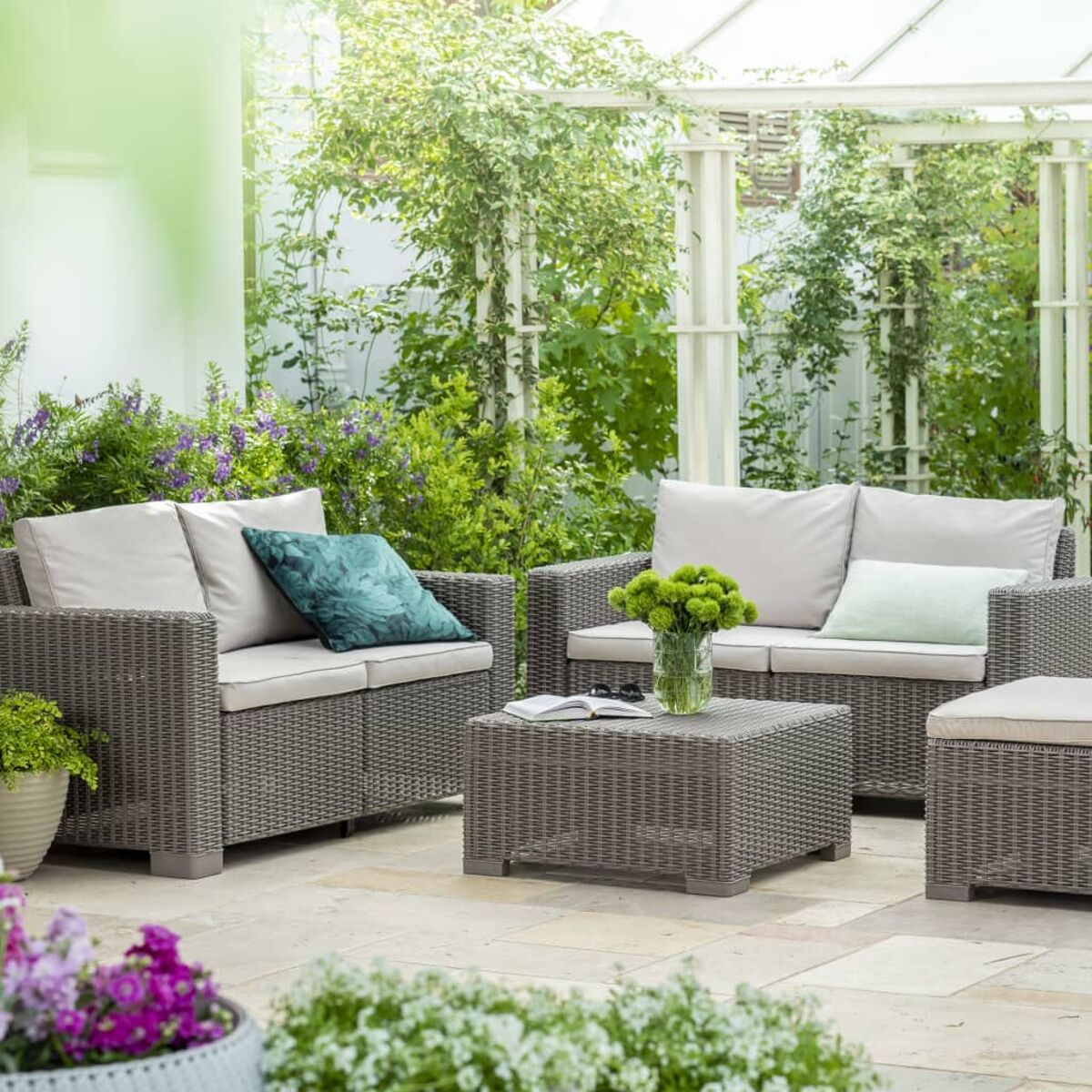 Un set divano da esterno in rattan grigio con un tavolino. L'ambientazione è su un patio.