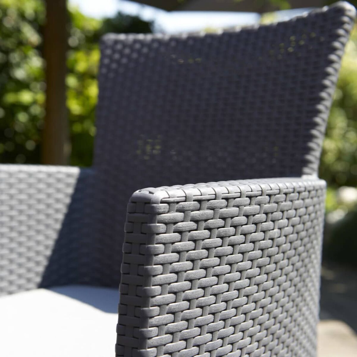 Nahaufnahme eines grauen Rattan-Stuhls mit weißem Kissen. Das Material hat ein Webmuster.