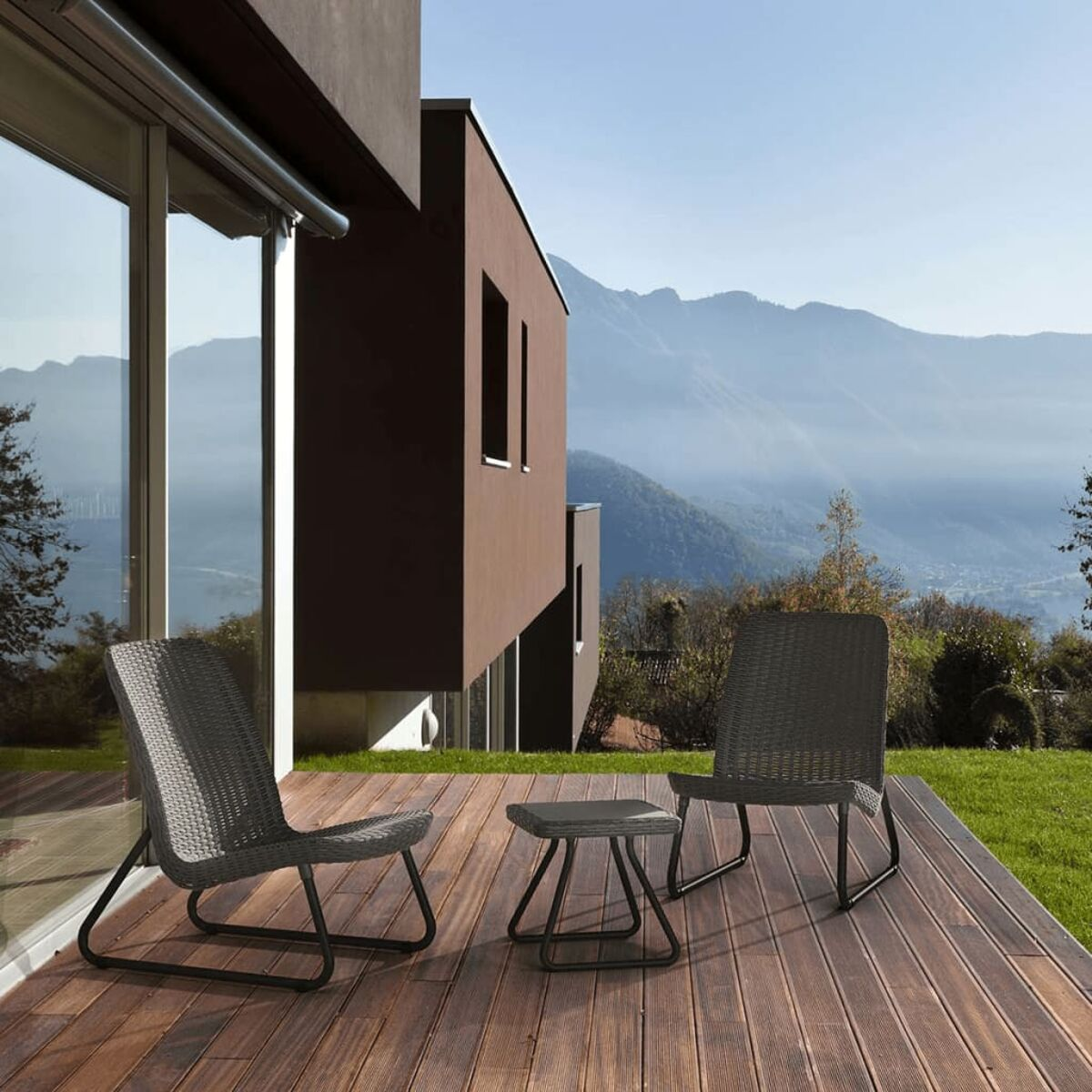 Zwei graue Rattan-Stühle und ein kleiner Tisch auf einem Holzdeck mit Bergblick.