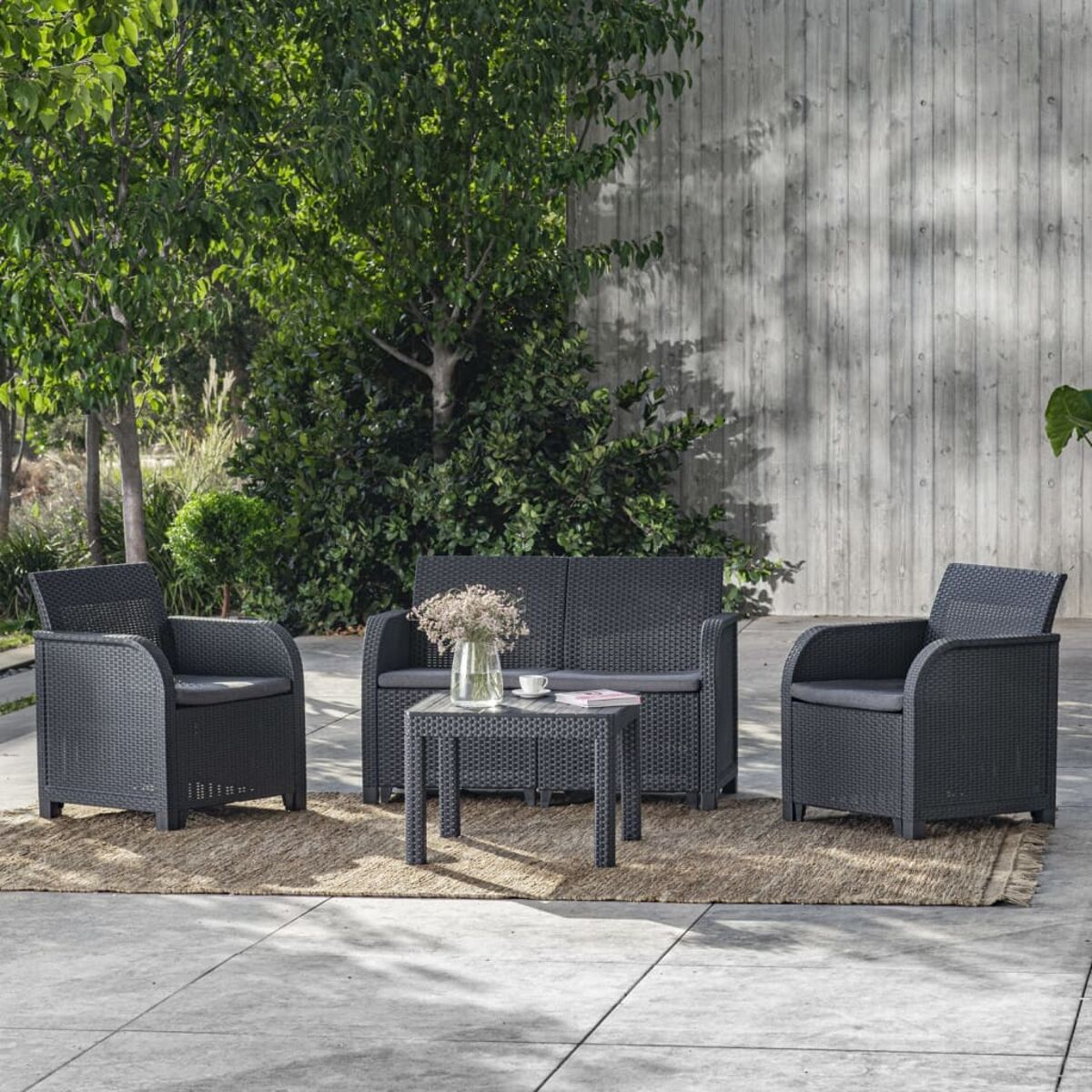 Gartenmöbel auf einer Steinterrasse. Enthält Sofa, zwei Stühle und einen Tisch.