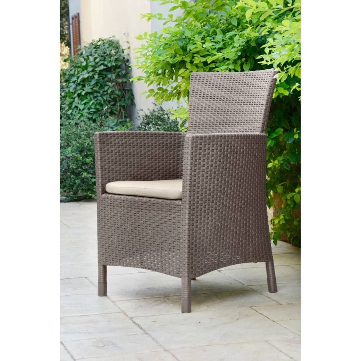 Sedia in vimini con cuscino beige. È all'aperto su pavimentazione in pietra.
