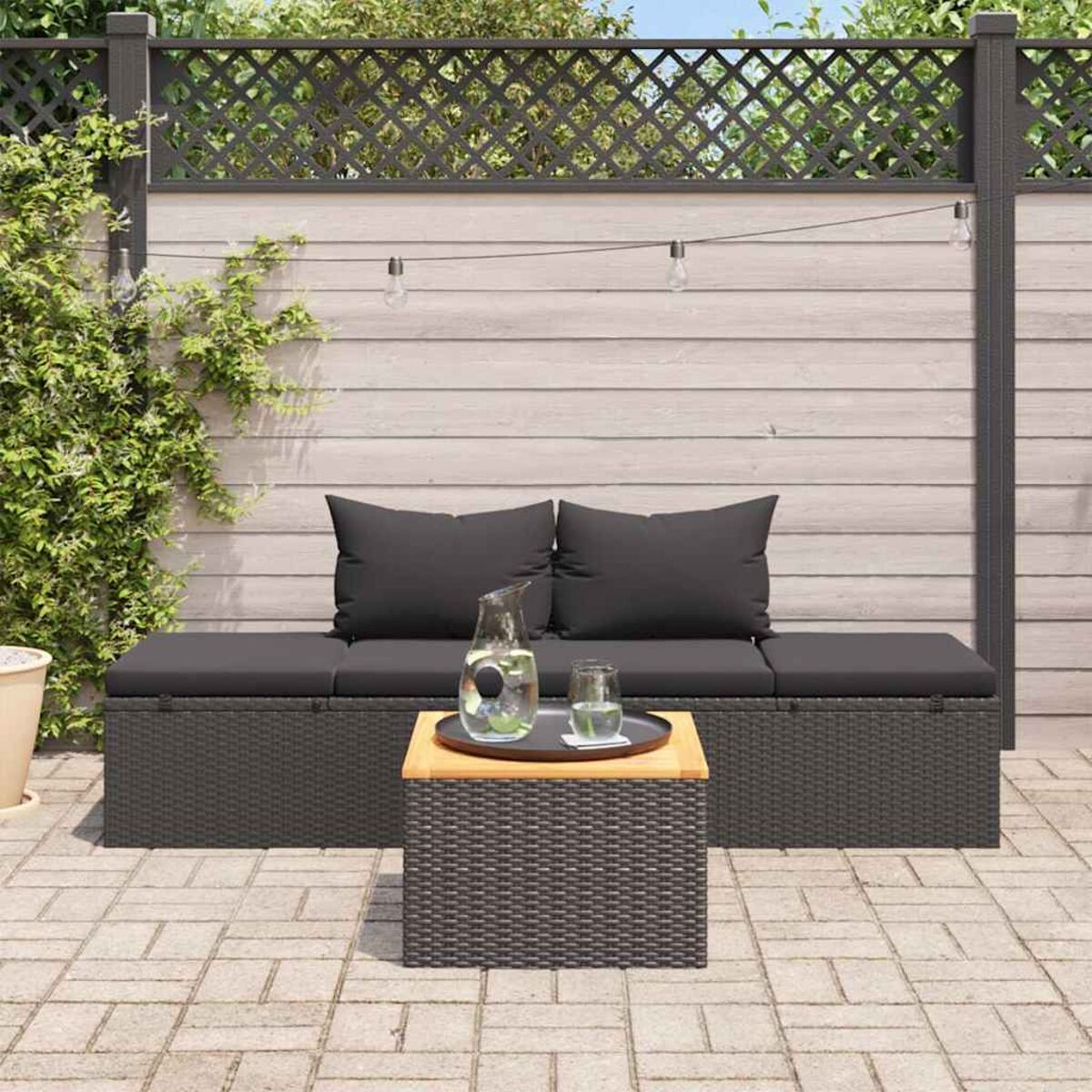 Außenbereich mit dunkelgrauem Ecksofa, Tisch und Pflanzen. Mit Zaunhintergrund.