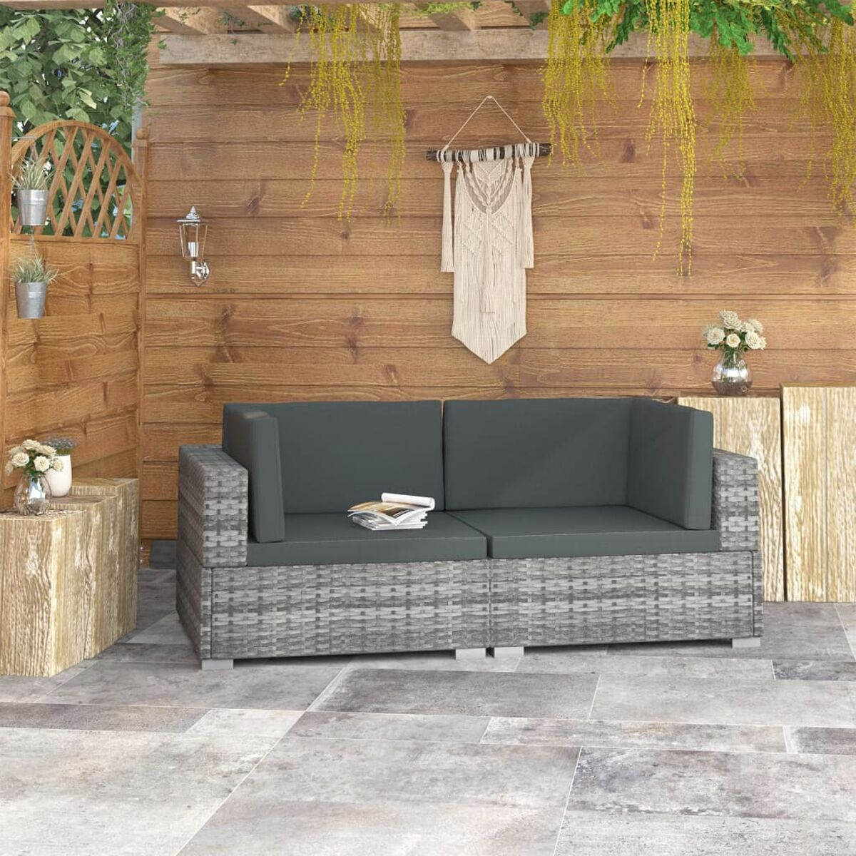 Terrassenmöbel mit grauem Sofa, Holzwand, Pflanzen und Makramee-Dekor.