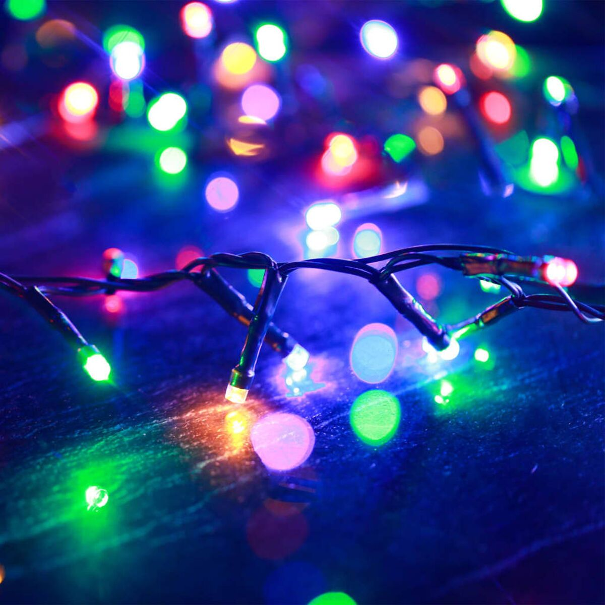 Nahaufnahme von bunten Weihnachtslichtern auf dunkler Oberfläche. Bokeh-Effekt.