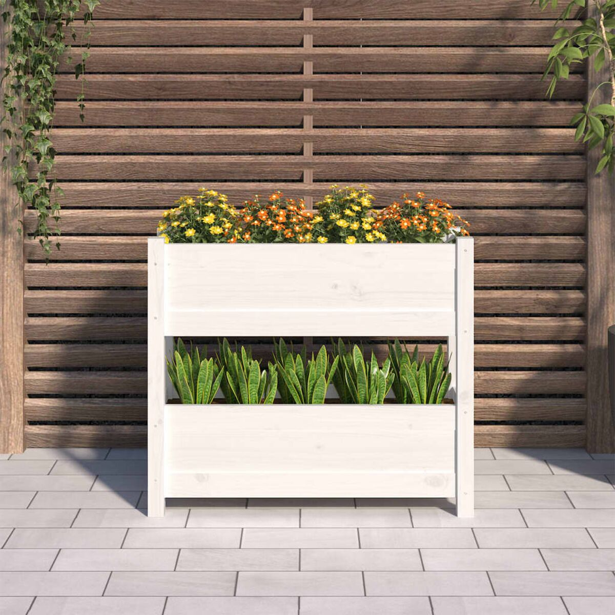 Ein weißer Pflanzkasten mit Blumen und Pflanzen, Holzzaun im Hintergrund.