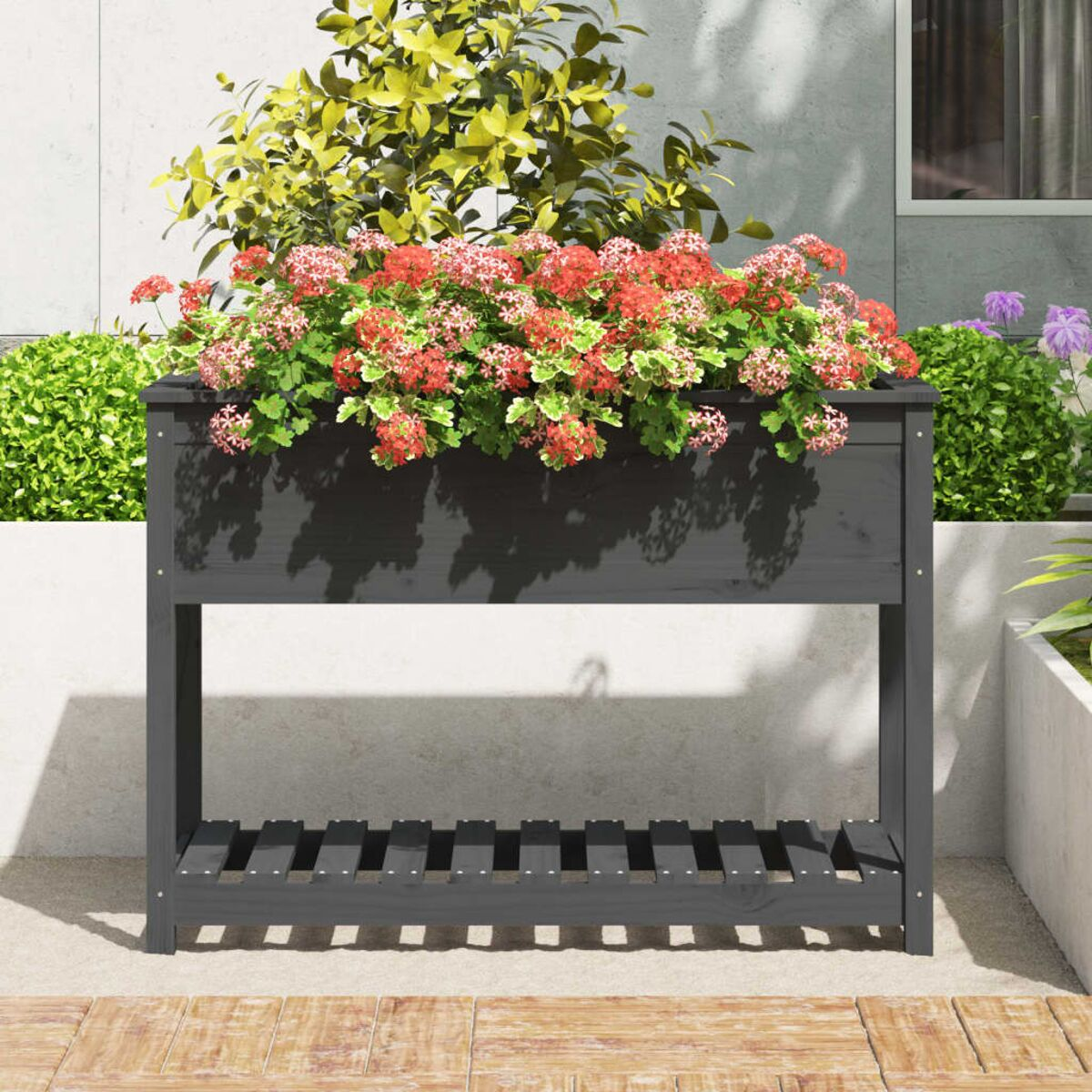 Eine dunkelgraue Pflanzkasten mit roten Blumen und grünem Laub. Der Pflanzer steht auf einer Terrasse.