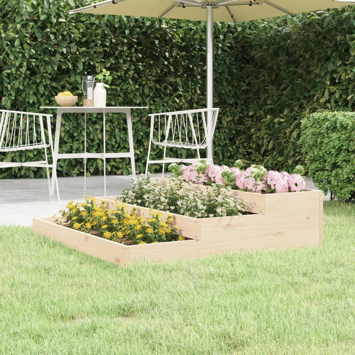 Gestufter Holzpflanzer mit Blumen in einem Garten. Tisch und Stühle im Hintergrund.