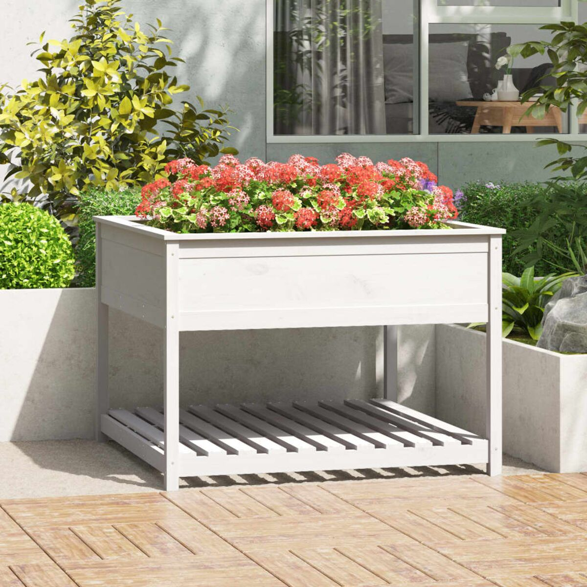 Weißer, erhöhter Pflanzkasten mit roten Blumen. Auf einem Holzdeck, mit hellem Hintergrund.