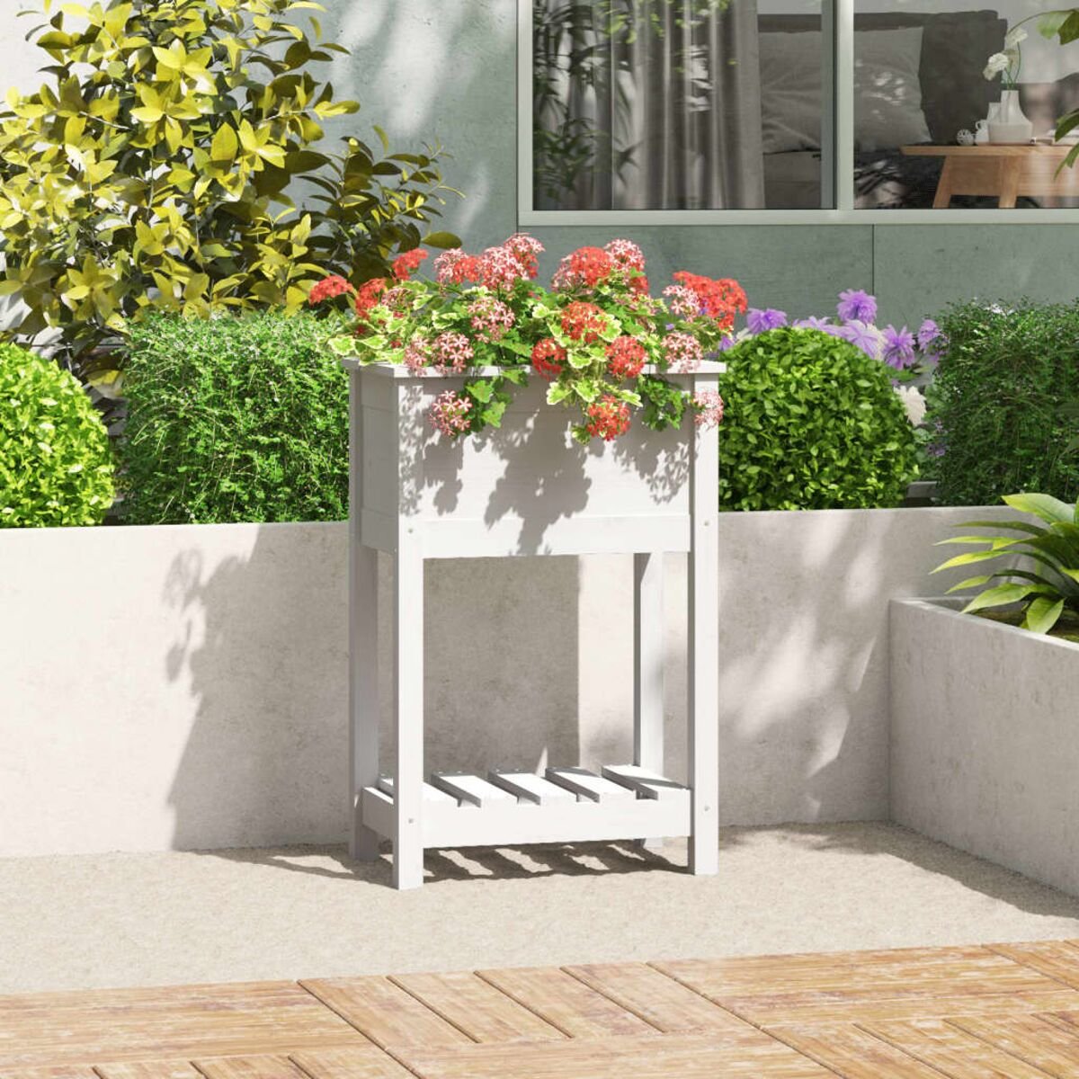 Weißer Pflanzkasten auf Beinen, gefüllt mit roten und rosa Blumen, auf einer Terrasse.