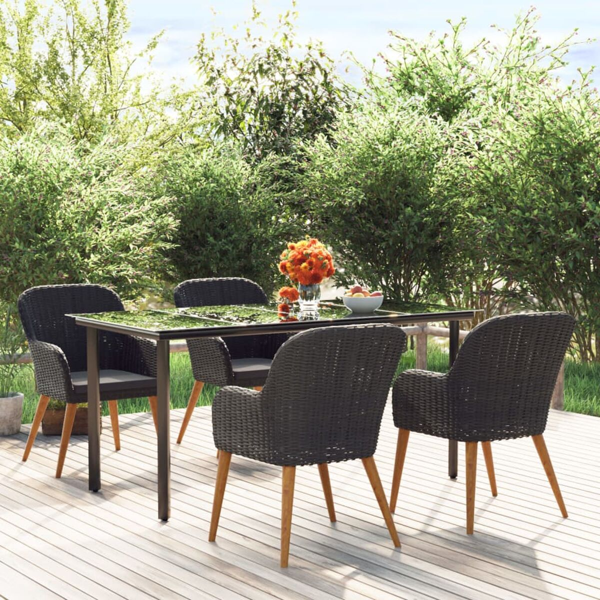 Ein Tisch mit vier Stühlen auf einer Holzterrasse mit Grün im Hintergrund.