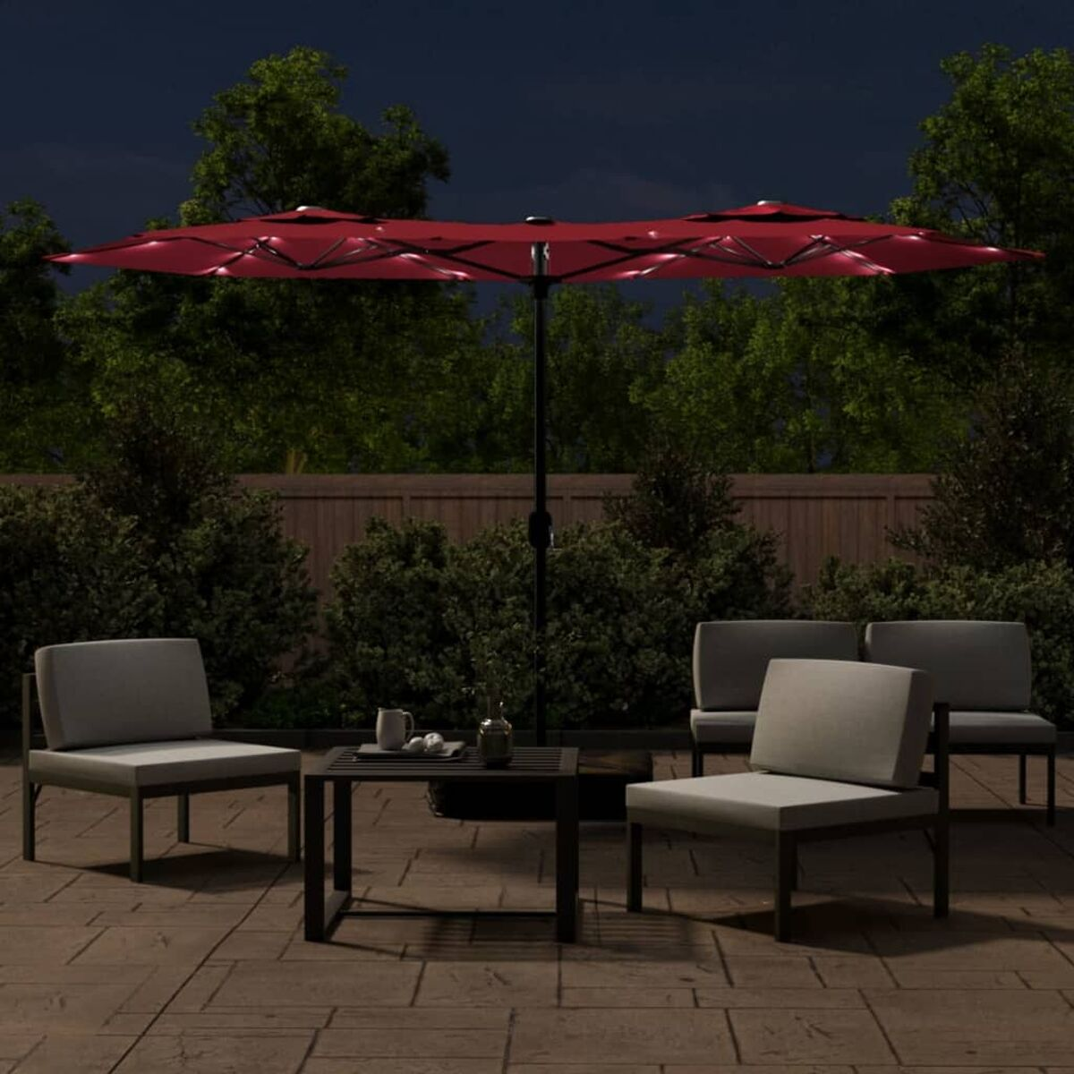 Ein rot beleuchteter Schirm über einem Tisch mit Stühlen in einem Garten bei Nacht. Der Schirm hat mehrere Lichter.
