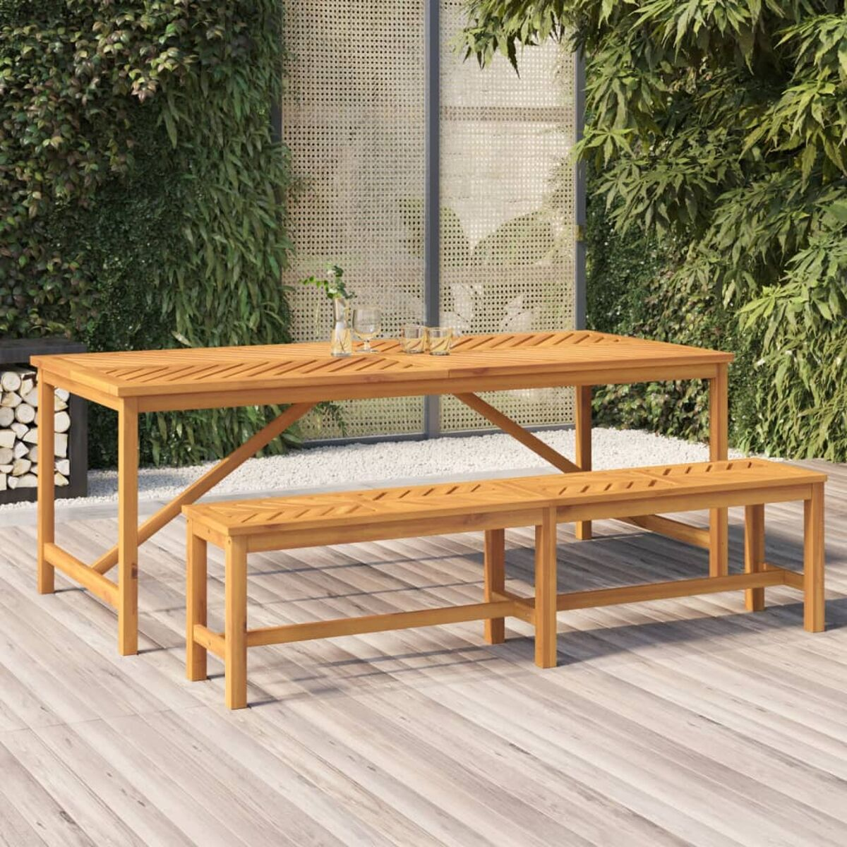 Holztisch und Bänke im Freien auf einer Holzterrasse, mit Grün im Hintergrund.