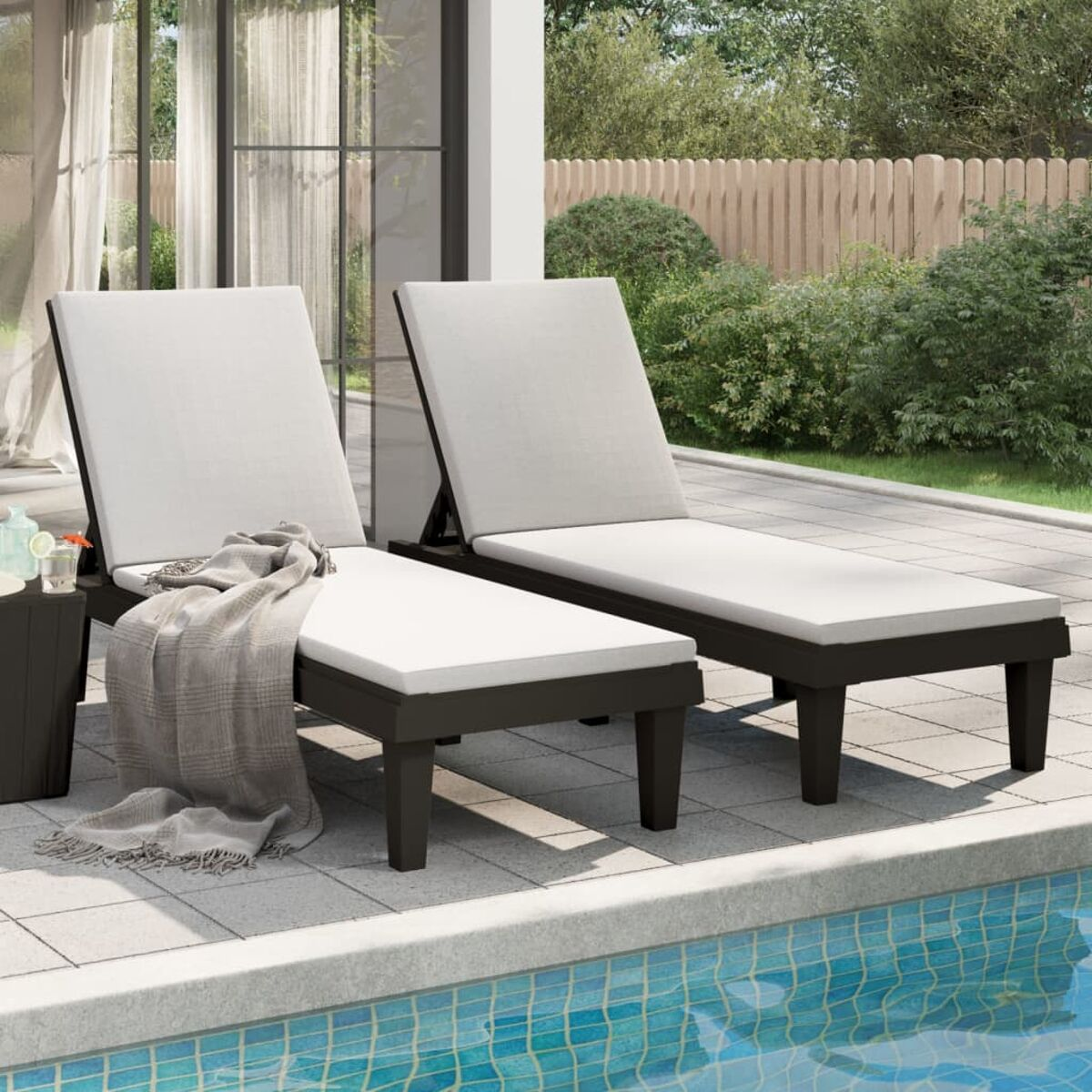 Zwei Outdoor-Liegen mit weißen Kissen in der Nähe eines Pools. Beinhaltet einen Beistelltisch und eine Decke.