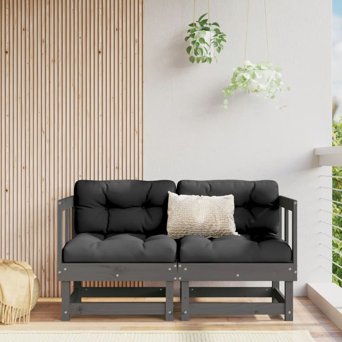 Zweisitzer-Graues Sofa mit schwarzen Kissen und einem beigen Kissen. Pflanzen und Holzverkleidung.