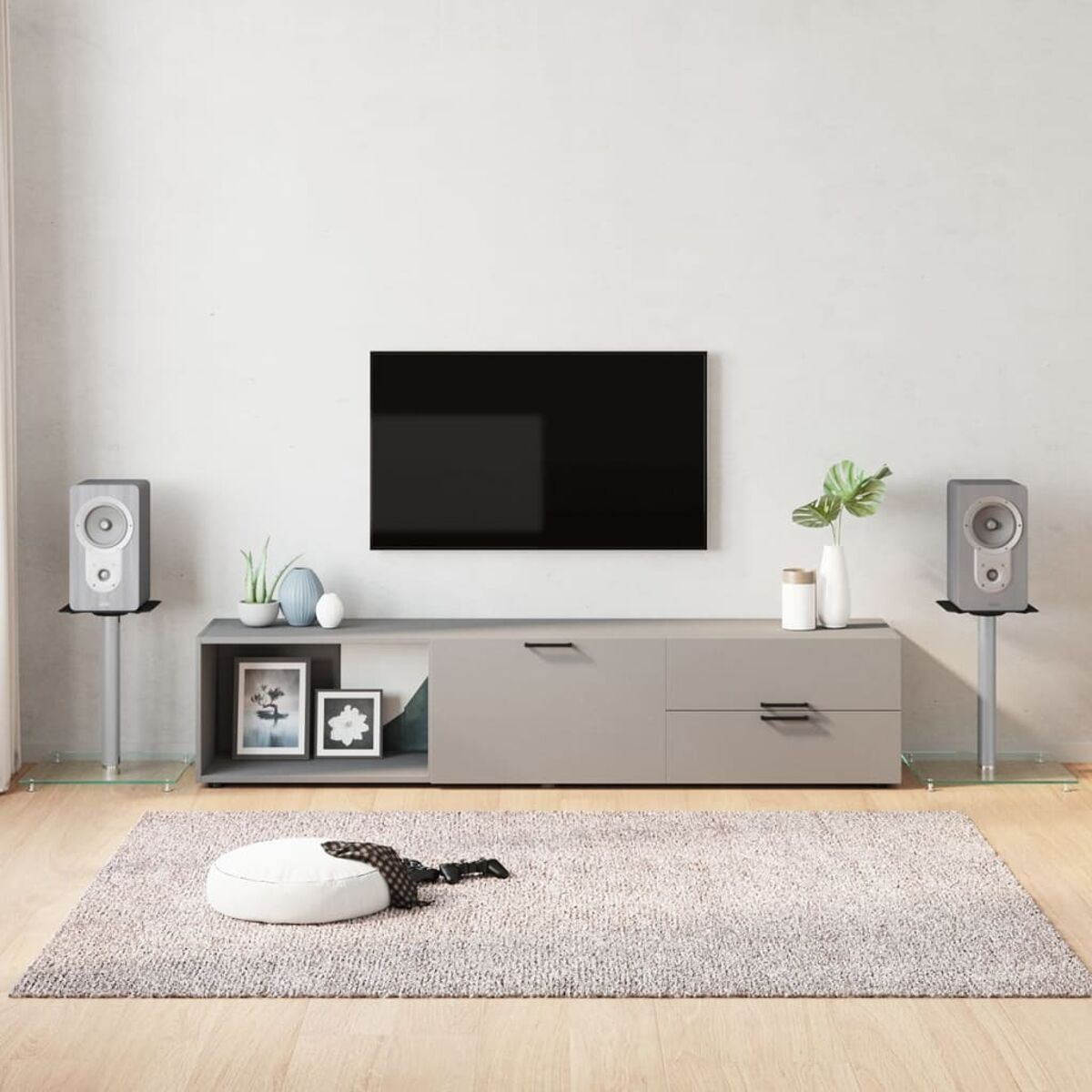 Modernes Wohnzimmer-Setup mit einem grauen TV-Ständer, Lautsprechern, einem Teppich und Dekorationsartikeln. Ein Fernseher hängt an der Wand.