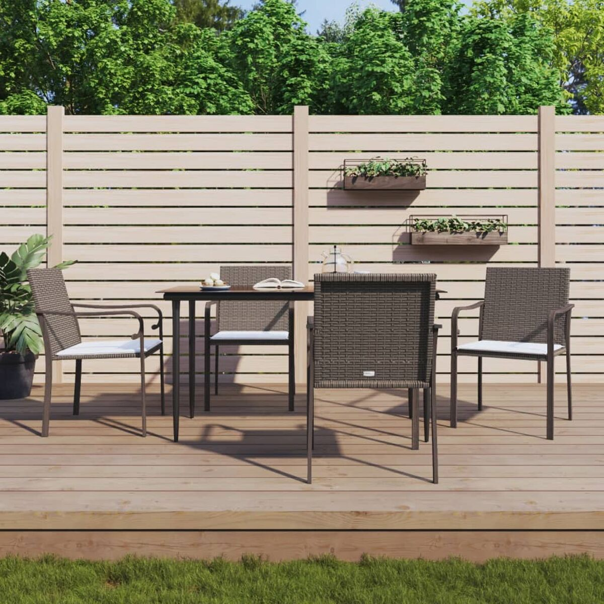 Terrassenset: Tisch mit vier Stühlen auf einem Holzdeck. Holzzaun und Grün im Hintergrund.