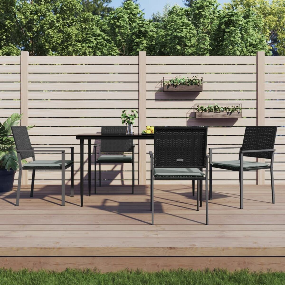 Terrassenset: Tisch und Stühle auf einem Holzdeck. Grün und Zaun im Hintergrund.