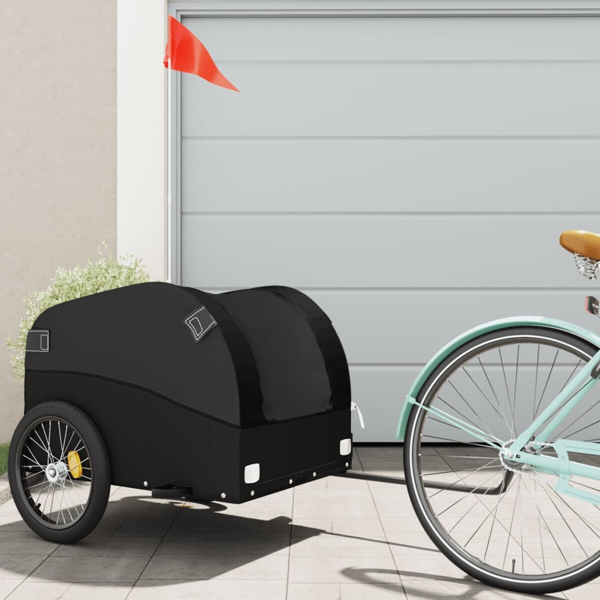 Ein schwarzer Fahrradanhänger mit roter Fahne. Ein blaues Fahrrad ist am Anhänger befestigt.