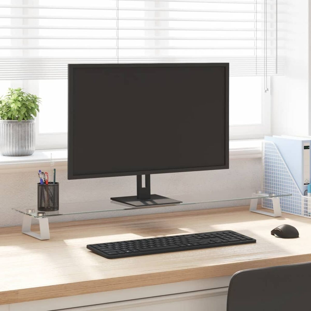 Computertisch mit Monitor, Tastatur und Zubehör. Im Hintergrund ein Fenster mit Jalousien.