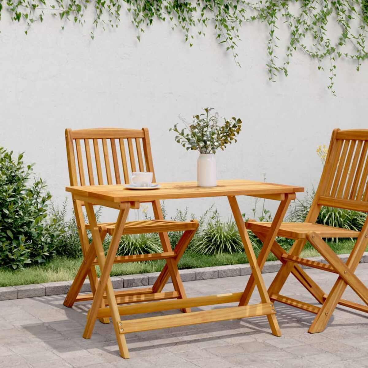 Holztisch mit zwei Stühlen, einer Vase mit Blumen und einer Teetasse auf einer Terrasse.
