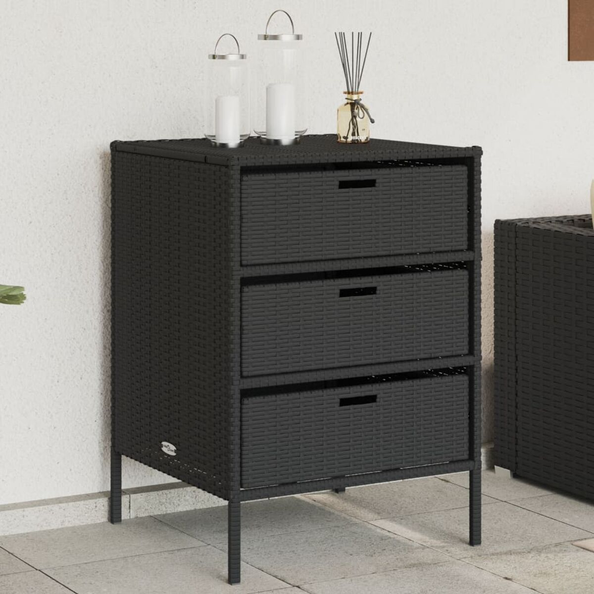 Schwarzer Korbschrank mit drei Schubladen. Zwei Kerzenhalter und Deko. Weißer Hintergrund.