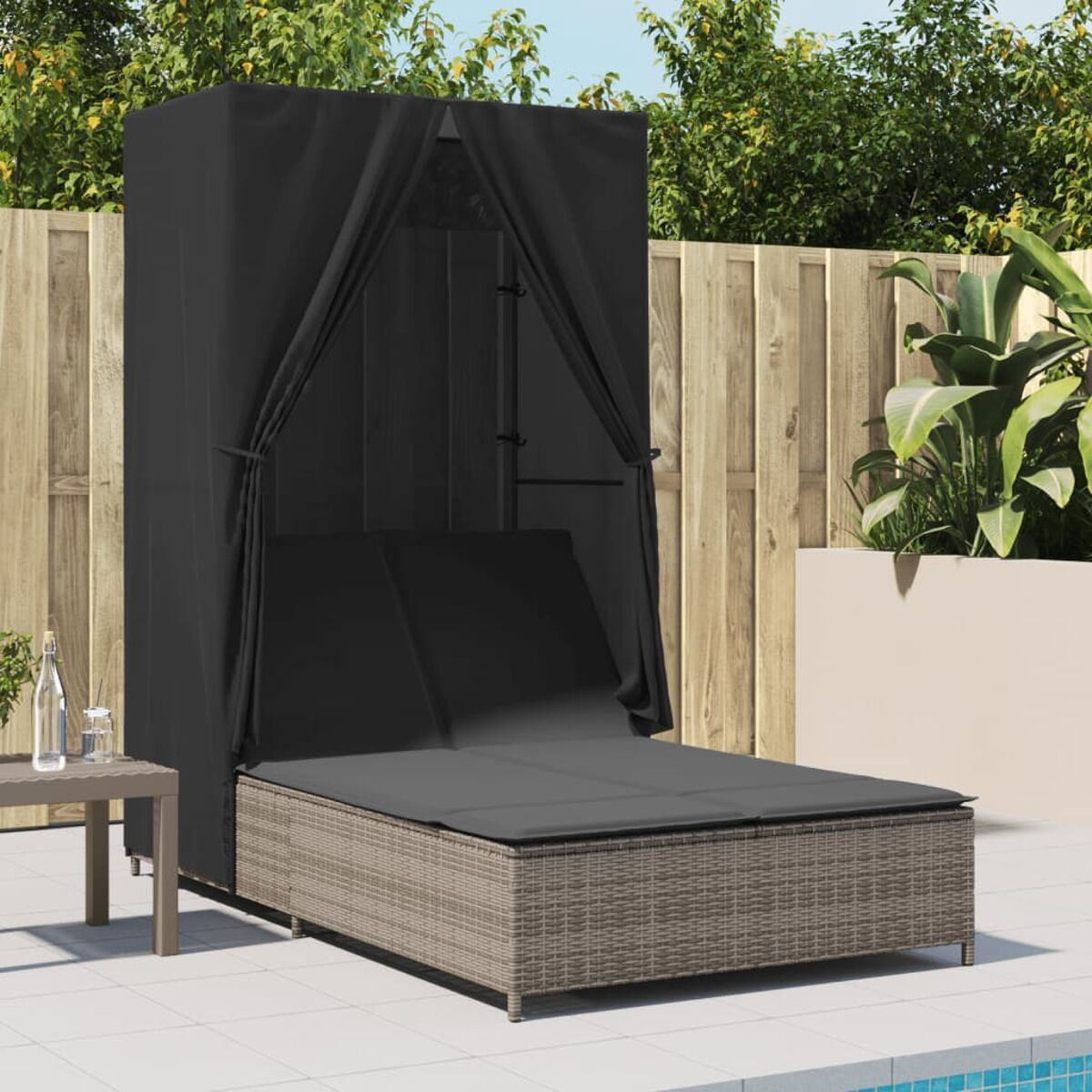Area lounge con due chaise longue, un tavolo e un baldacchino nero. Mobili in vimini marrone.