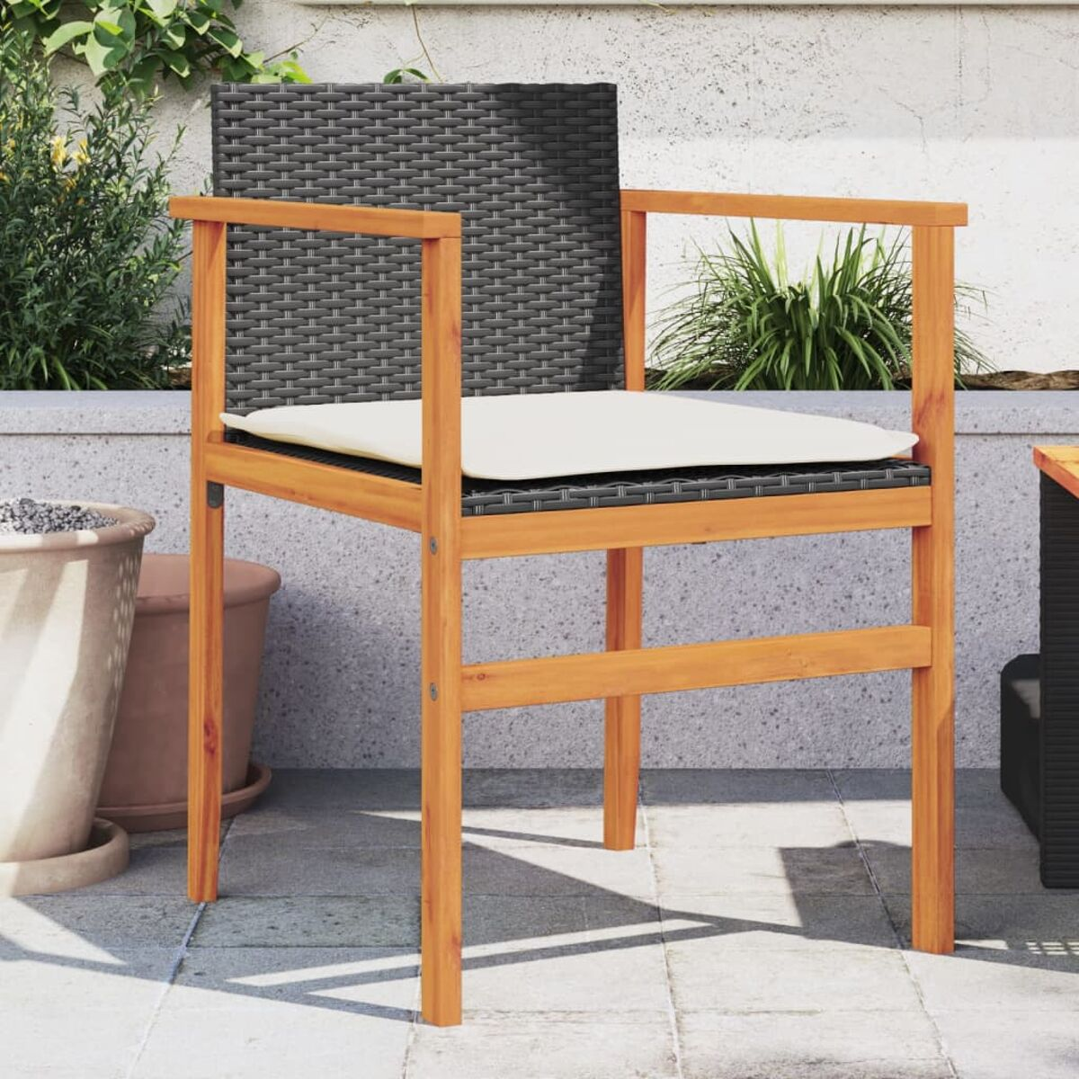 Ein Holzstuhl mit schwarzem, gewebtem Sitz und einem beigen Kissen, auf einer Terrasse mit Pflanzen.