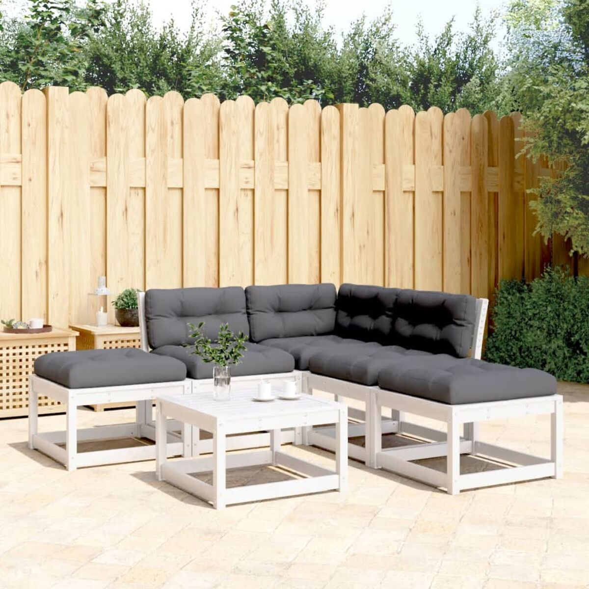 Weißes Outdoor-Ecksofa mit grauen Kissen und Couchtisch. Hintergrund: Holzzaun.