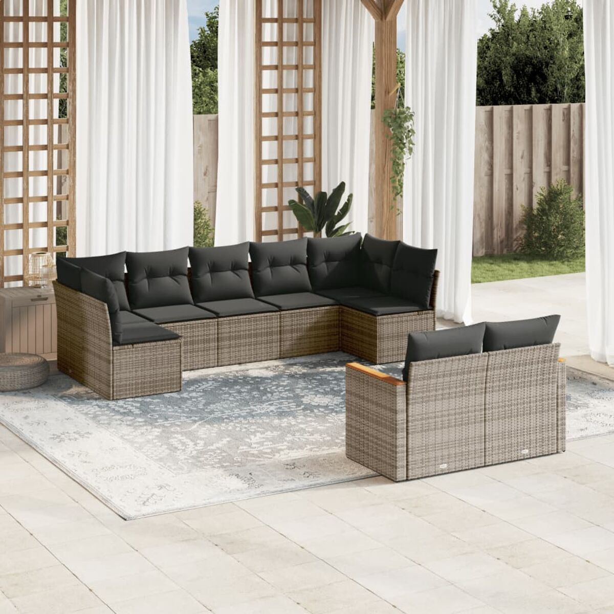 Geflochtenes Outdoor-Sofa mit schwarzen Kissen. Es steht auf einer Terrasse mit weißen Vorhängen.