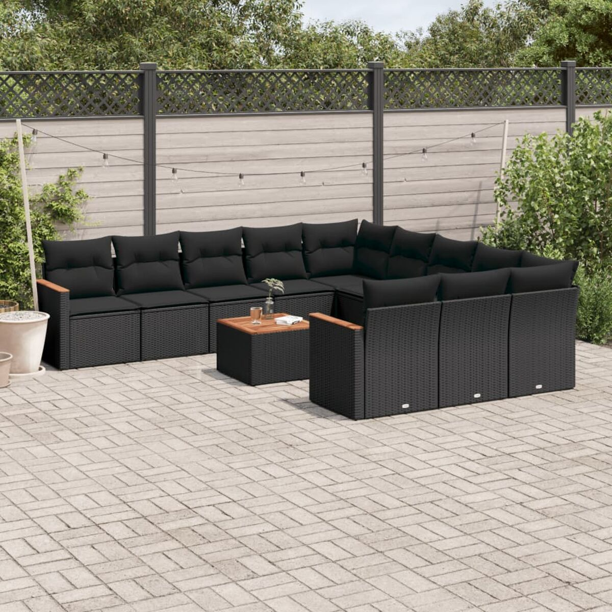 Schwarzes Rattan-Ecksofa-Set mit schwarzen Kissen, auf einer gepflasterten Terrasse, mit einem Couchtisch.