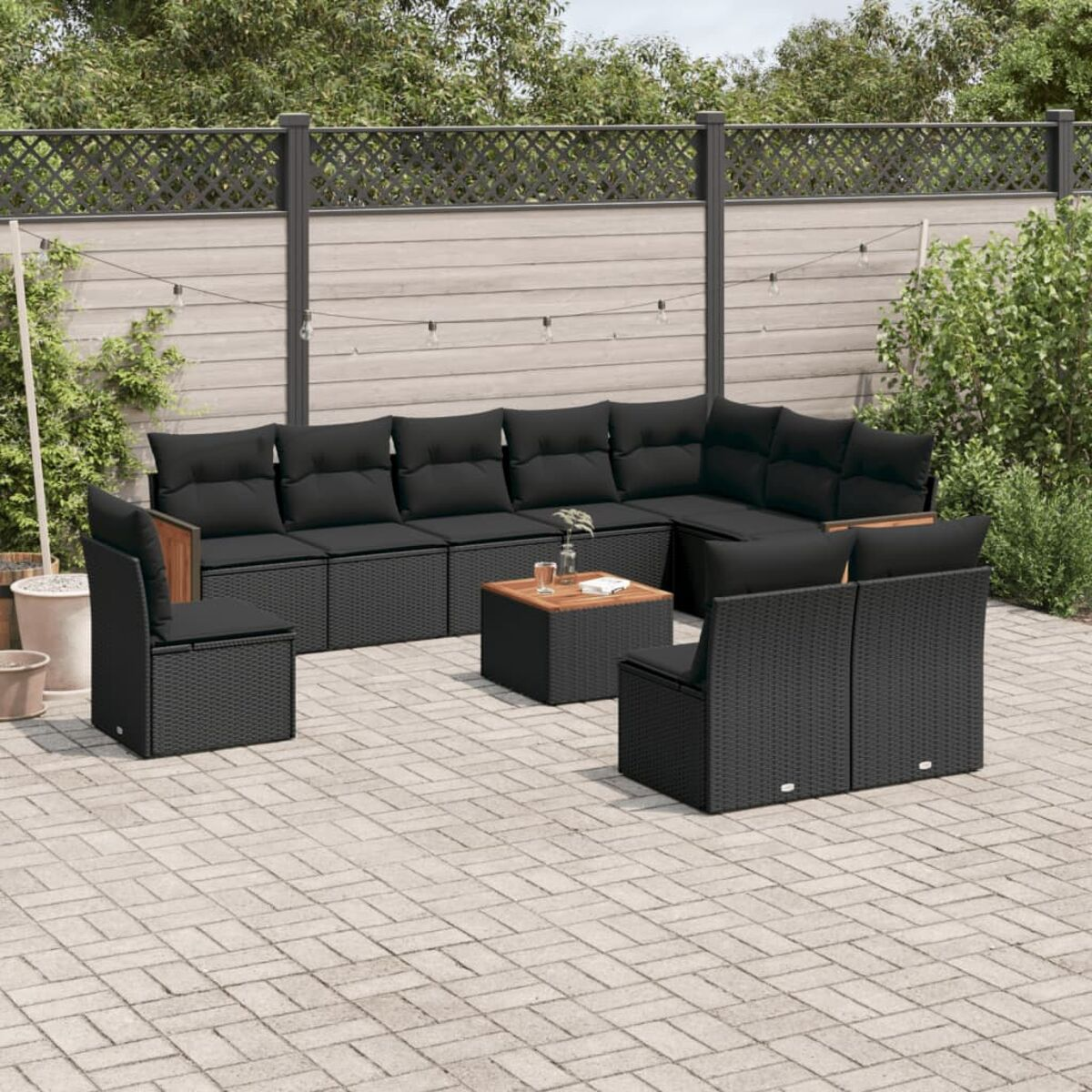 Ein schwarzes Outdoor-Terrassenset mit schwarzen Kissen und einem Holztisch auf einer Ziegelterrasse.