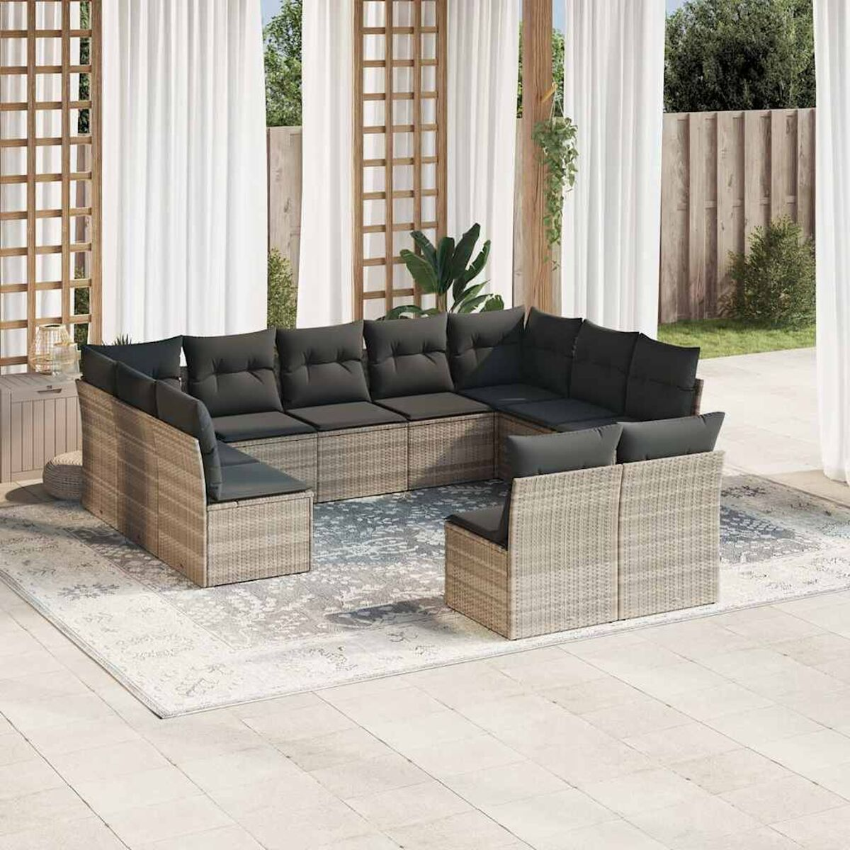 U-förmiges Outdoor-Geflecht-Sofagarnitur mit dunkelgrauen Kissen auf einem gemusterten Teppich. Weiße Vorhänge.
