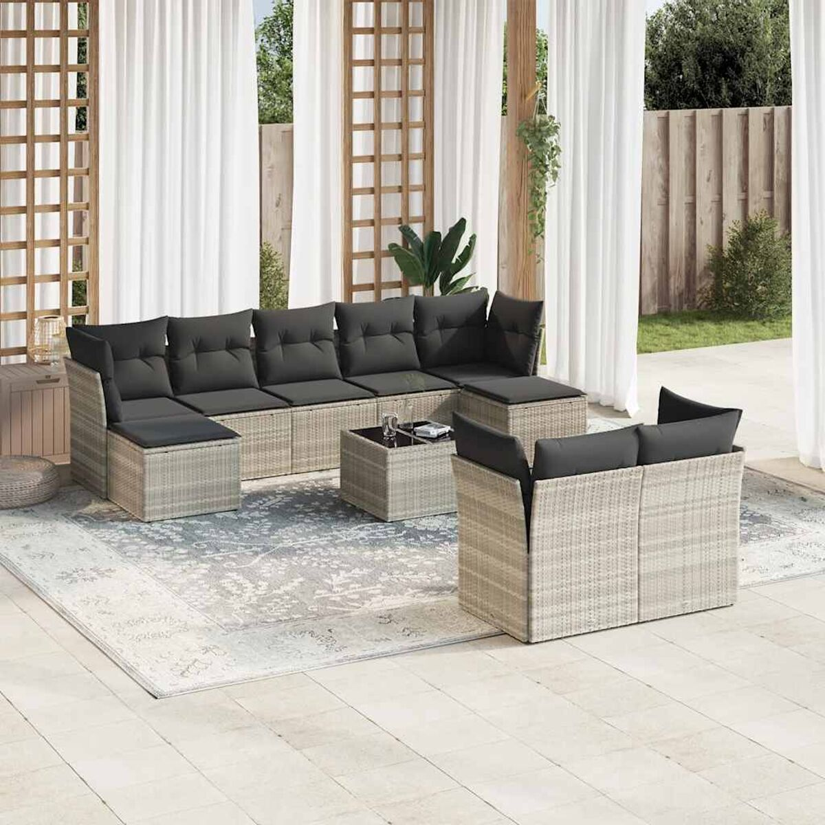 Gartenset: helles Korbmöbel mit dunklen Kissen, Teppich, Holzgitter und weiße Vorhänge.