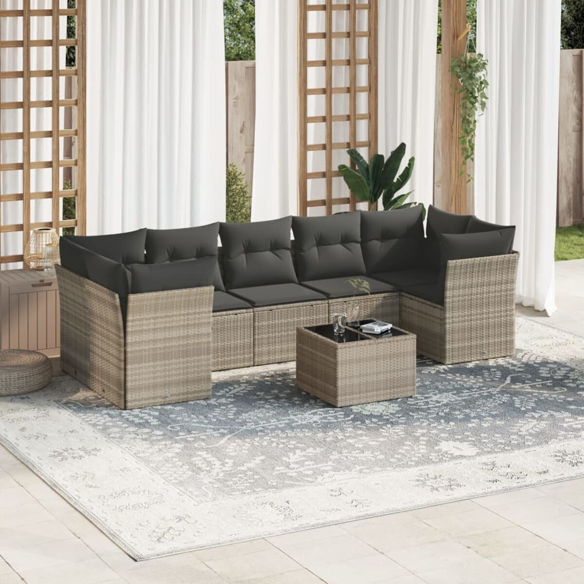 Rattan-Garnitur für den Außenbereich mit grauen Kissen. Terrasse mit Vorhängen, Glastisch.