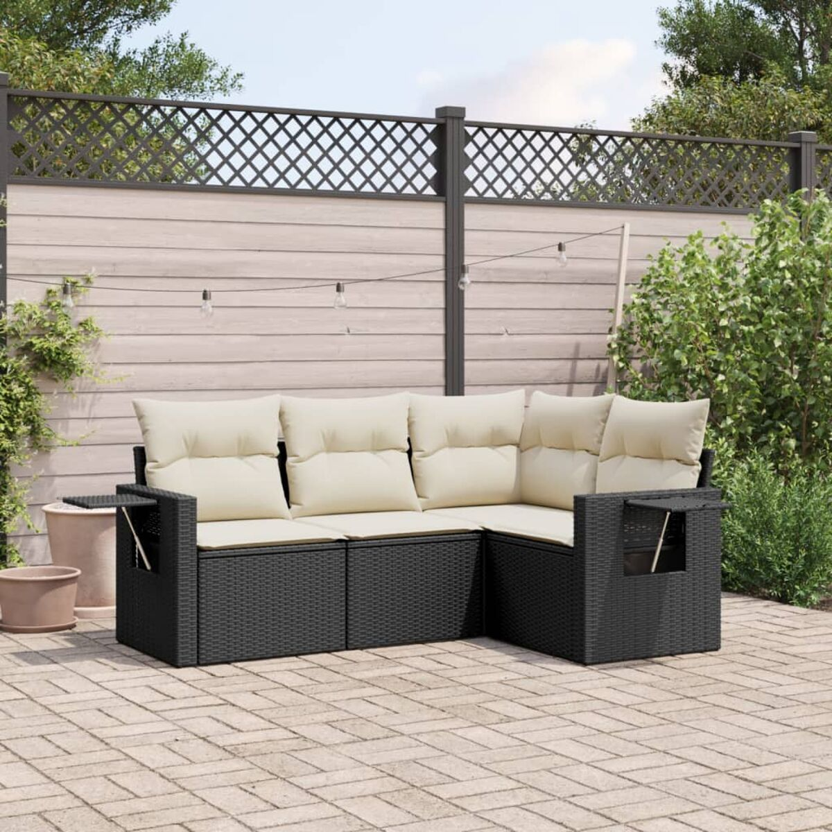 Schwarzes Outdoor-Sofaset mit cremefarbenen Kissen. Szene ist in einem Garten mit Zaun und Pflanzen.