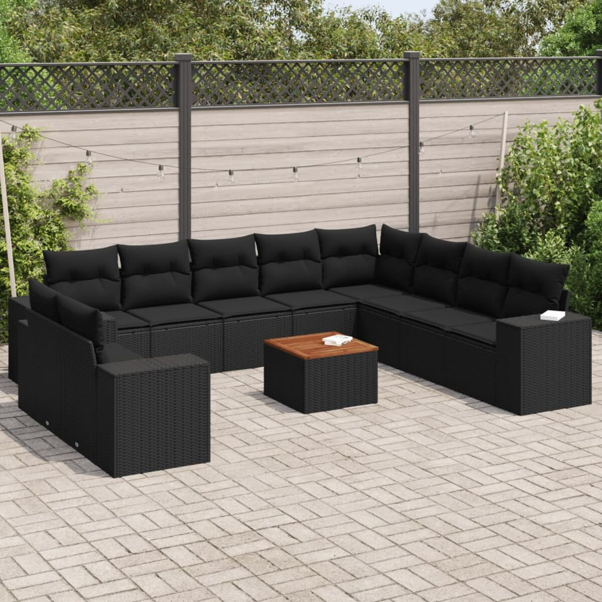 Schwarzes Rattan-Ecksofa und Couchtisch auf einer Terrasse. Hintergrund: Zaun und Pflanzen.