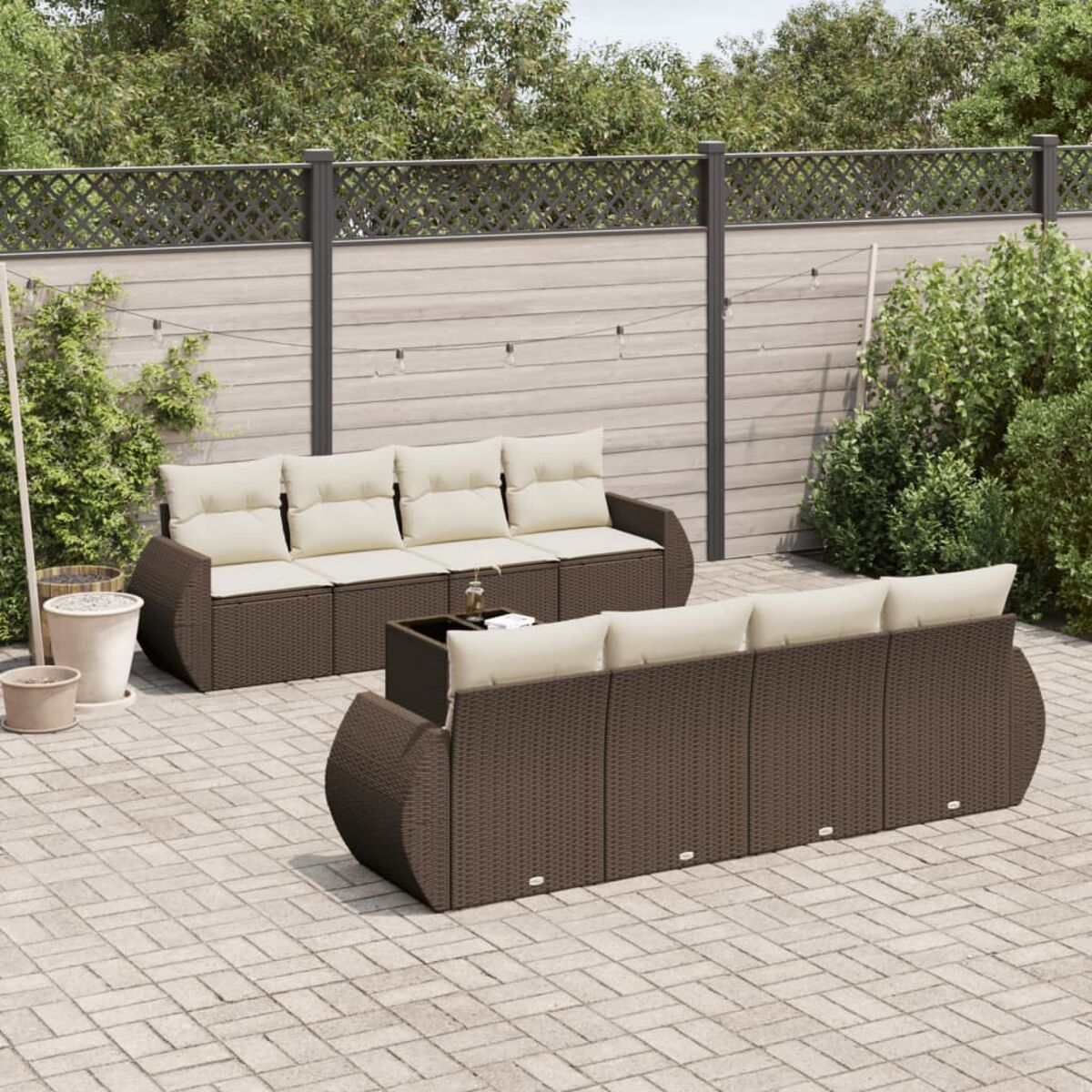 Divani da esterno in vimini marrone con cuscini beige. Sfondo con recinzione e verde.