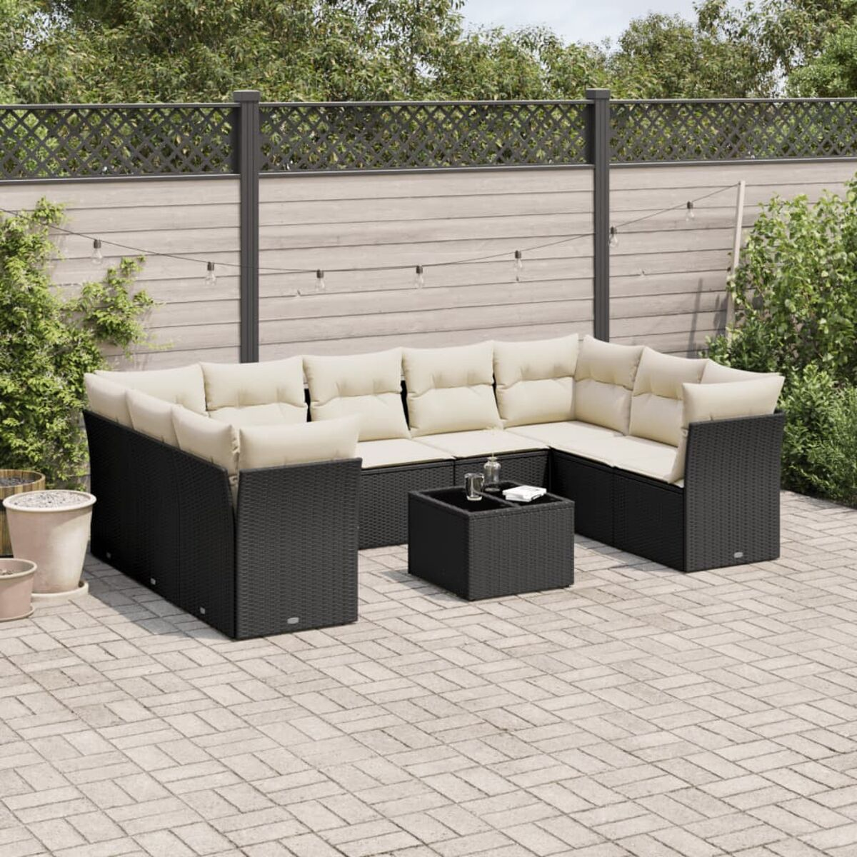 Schwarzes Ecksofa aus Korbgeflecht mit cremefarbenen Kissen und einem quadratischen Tisch auf einer Terrasse.