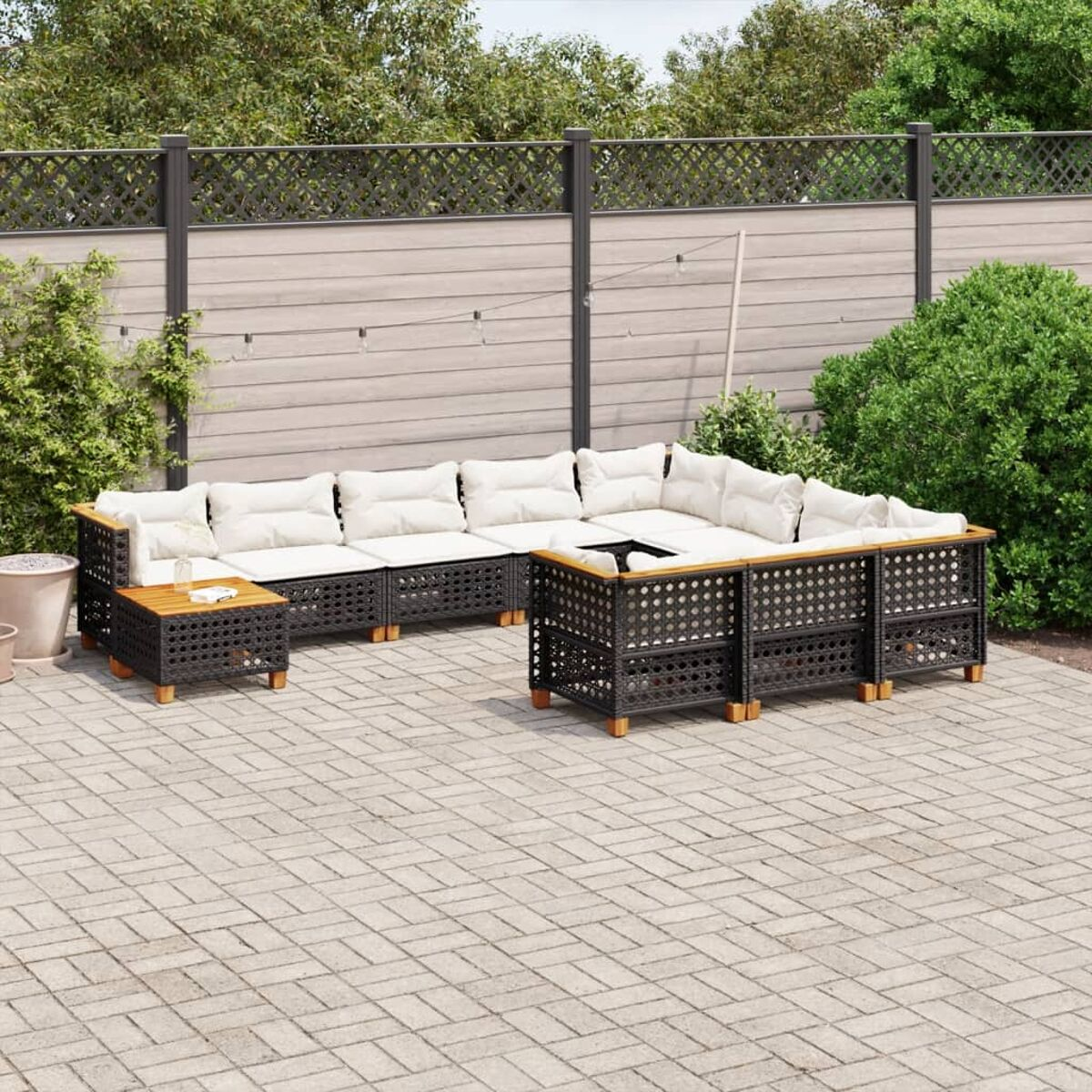 Dunkle Rattan-Gartenmöbel. Ecksofa, Tisch und ein zweites Sofa. Weiße Kissen sichtbar.