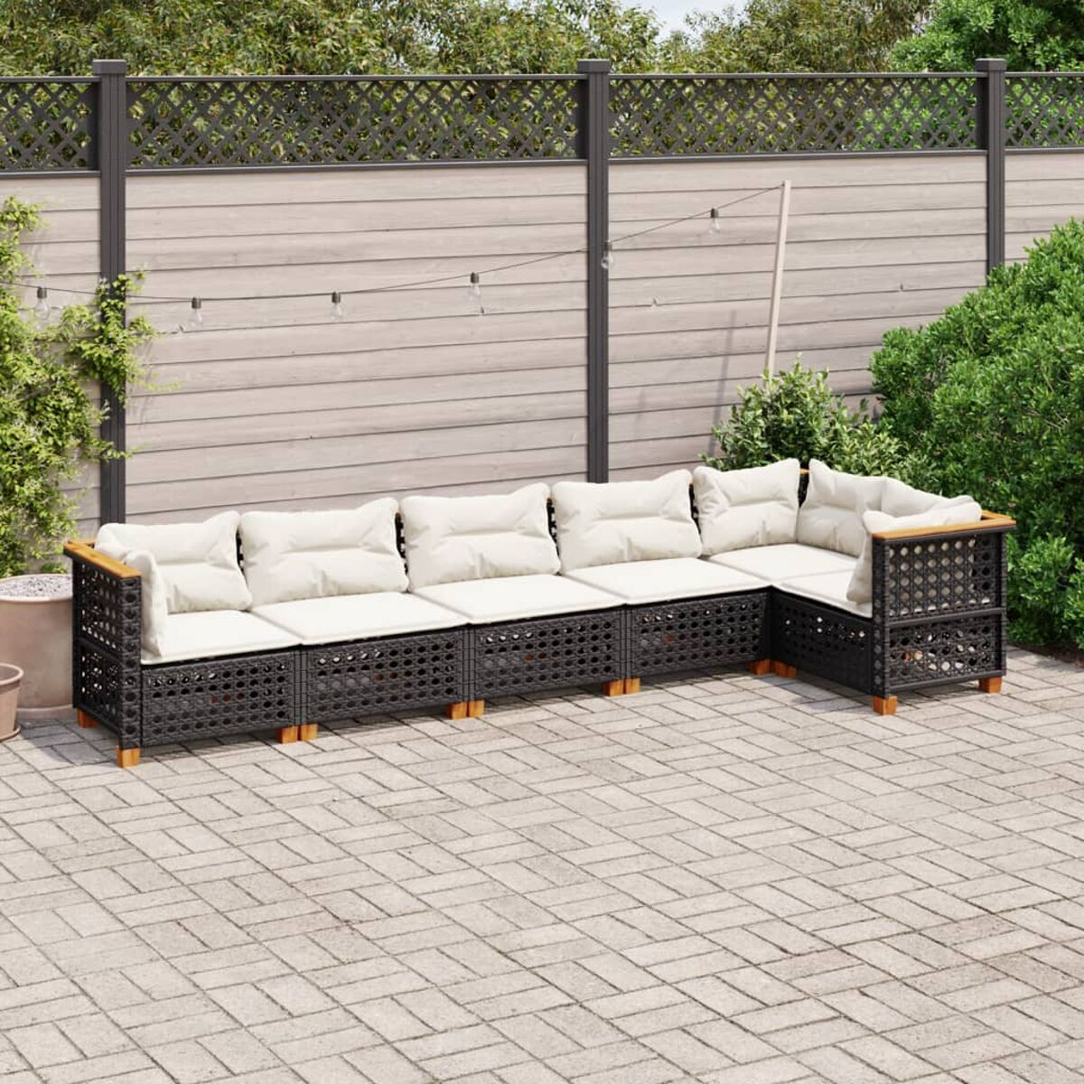 Ein Outdoor-Sofa aus schwarzem Korbgeflecht auf einer Terrasse. Weiße Kissen und Holzakzente sind sichtbar.