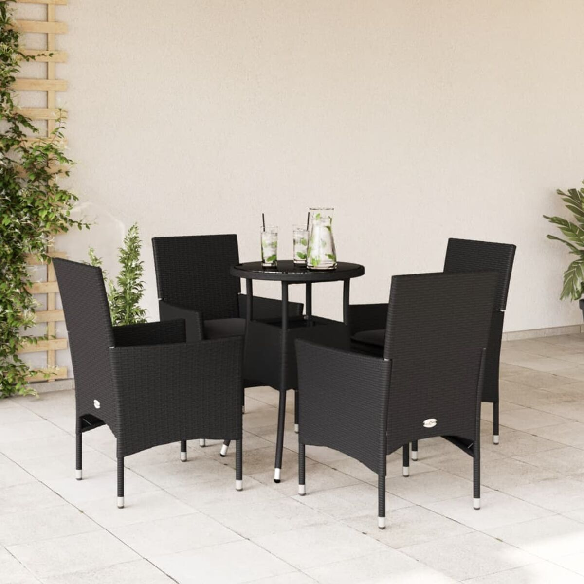 Vier schwarze Stühle um einen schwarzen Tisch mit Getränken. Weiße Wand und Laub im Hintergrund.