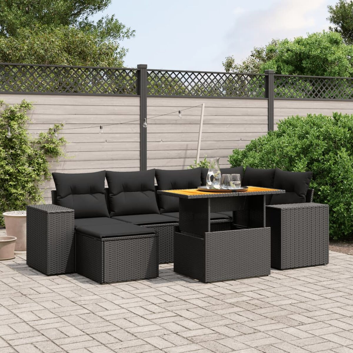 Schwarzes Outdoor-Ecksofa aus Korbgeflecht mit Tisch und Ottomanen. Die Umgebung ist auf Steinplatten.