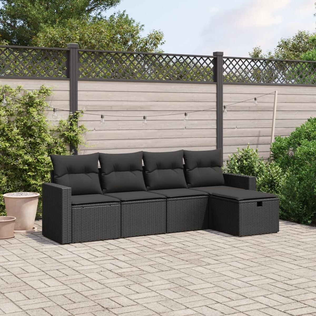 Schwarzes Korbmöbel-Sofa mit Kissen und passendem Ottomanen. Im Hintergrund ein Holzzaun.