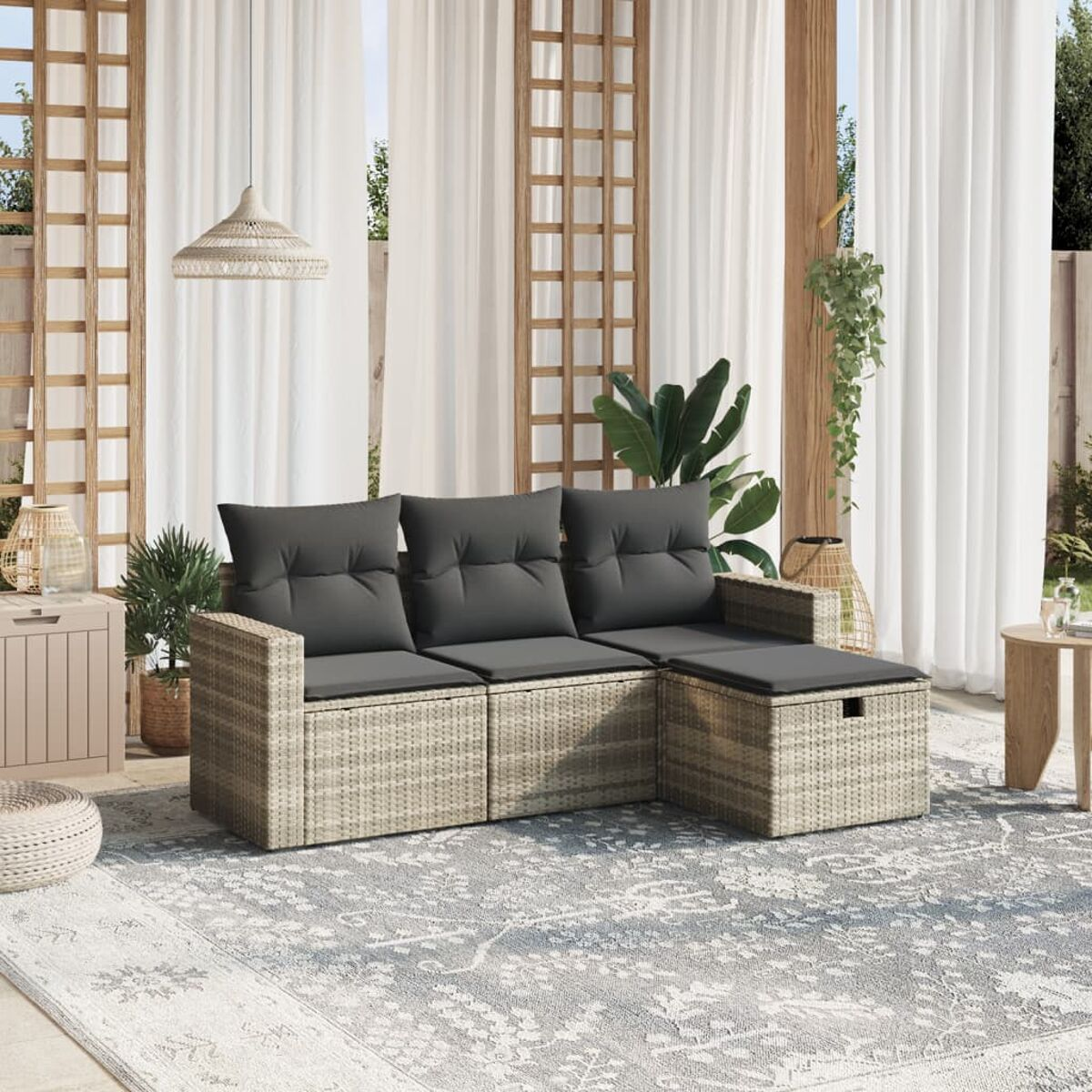 Terrasse im Freien mit einem hellen Korbmöbel-Set, grauen Kissen und einem Teppich. Pflanzen und Vorhänge sind im Hintergrund.