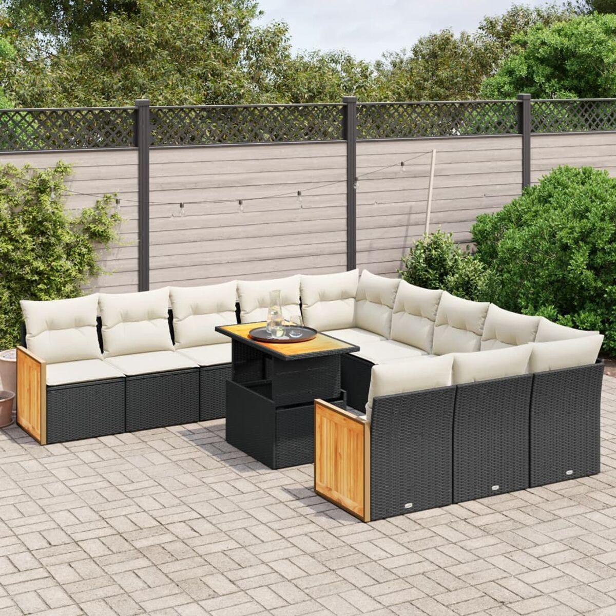Outdoor-Ecksofa in Schwarz mit einem Couchtisch aus Holz. Ziegelterrasse, Grün im Hintergrund.