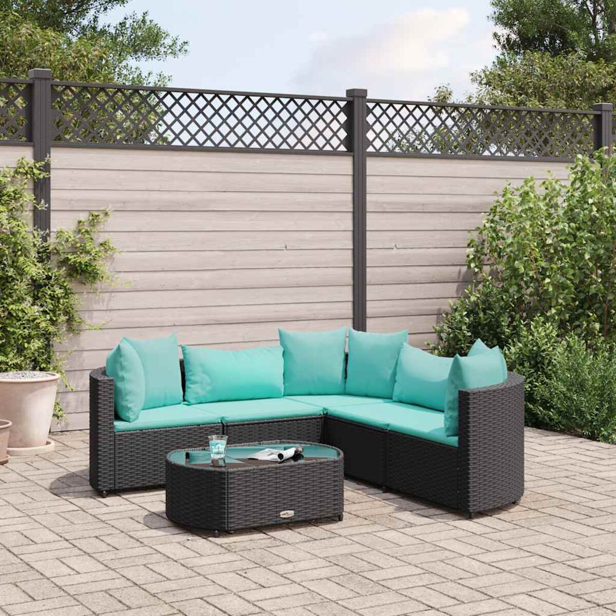 Divano componibile in rattan nero con cuscini turchesi e un tavolo rotondo. È su un patio in mattoni.
