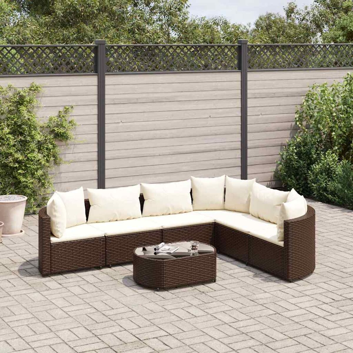Set da patio esterno con divani in vimini marrone scuro, un tavolino e cuscini bianchi. Una recinzione sullo sfondo.
