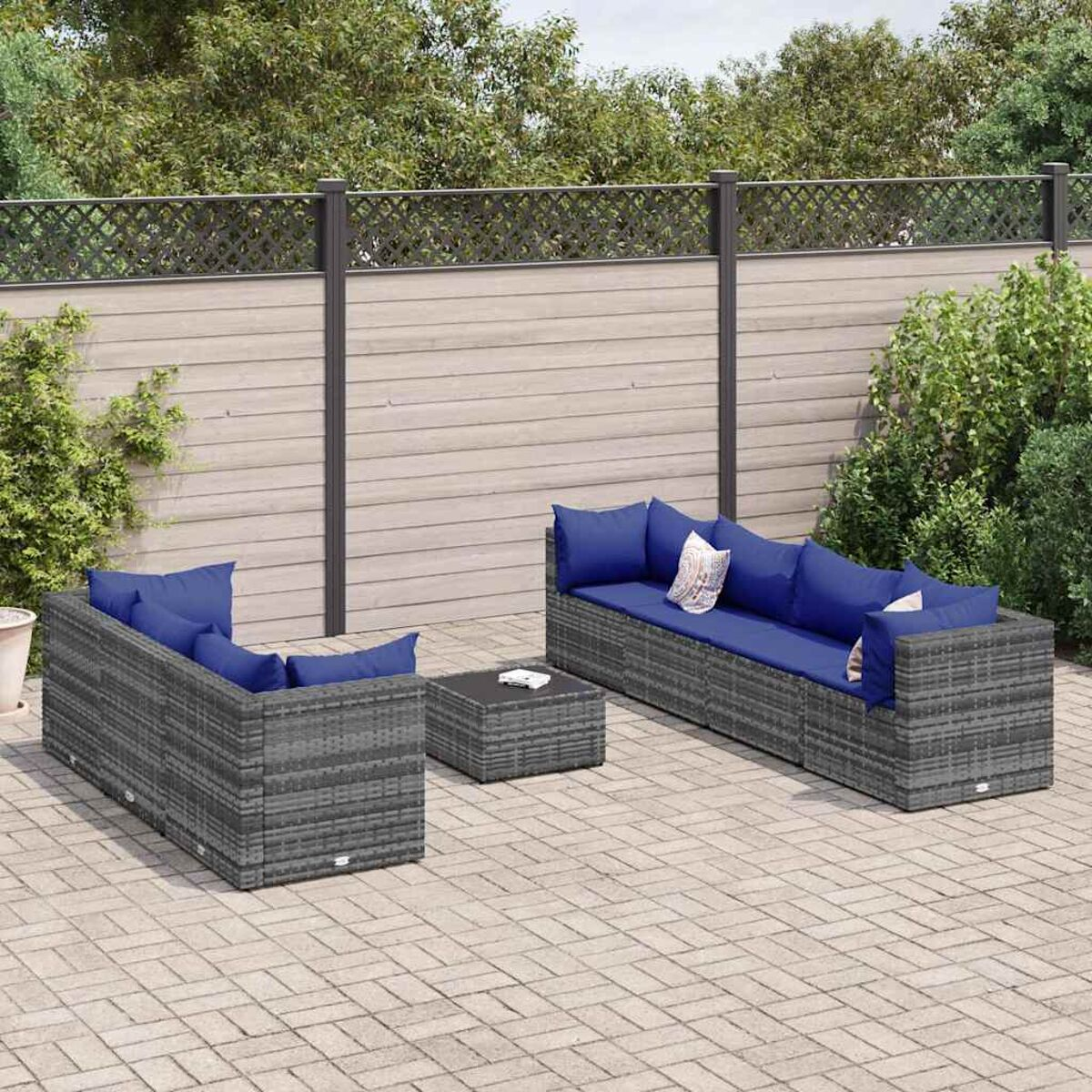 Gartenmöbel-Set: graues Rattansofa, Liege und Couchtisch mit blauen Kissen, auf einer Terrasse.